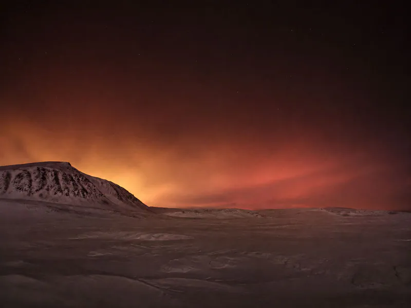 Snowfield and ridge beneath a faint aurora at night.
